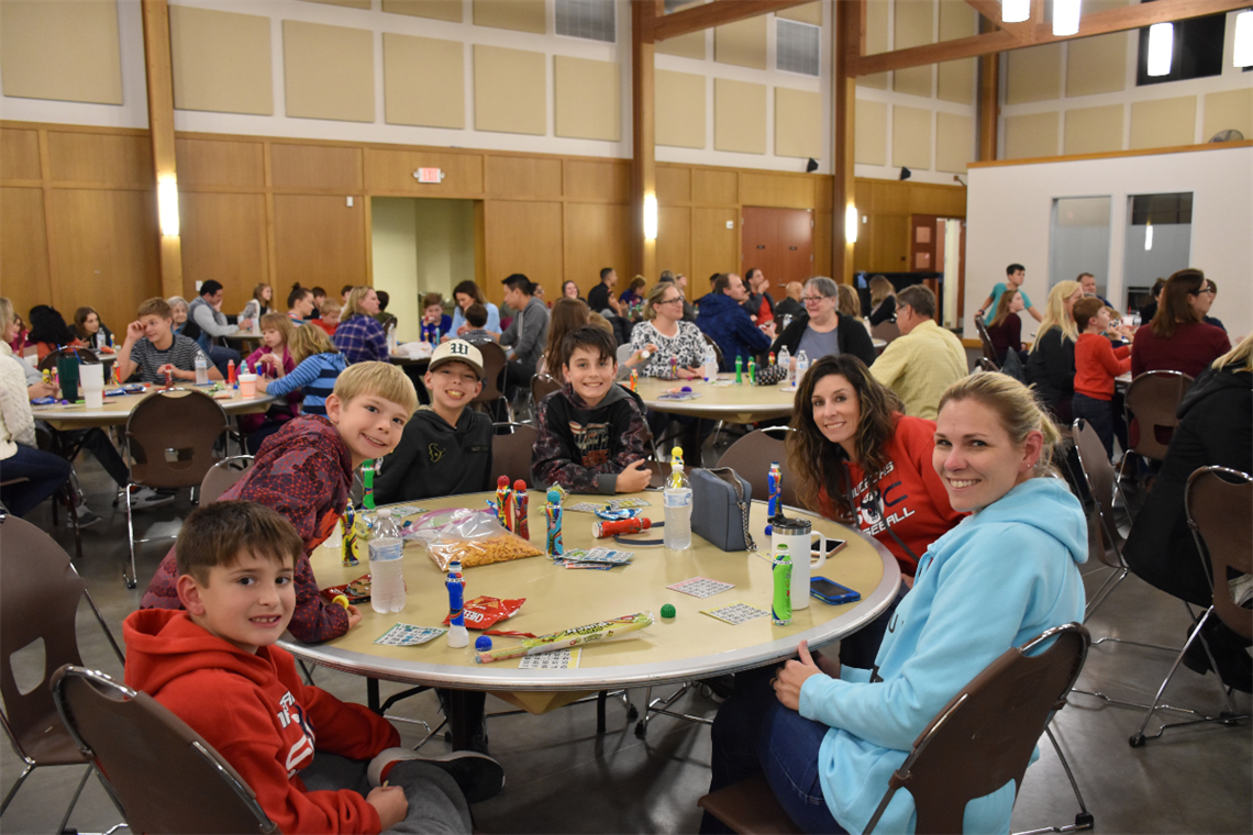 Photo of children and adults sitting at a round table with Bingo cards and snacks