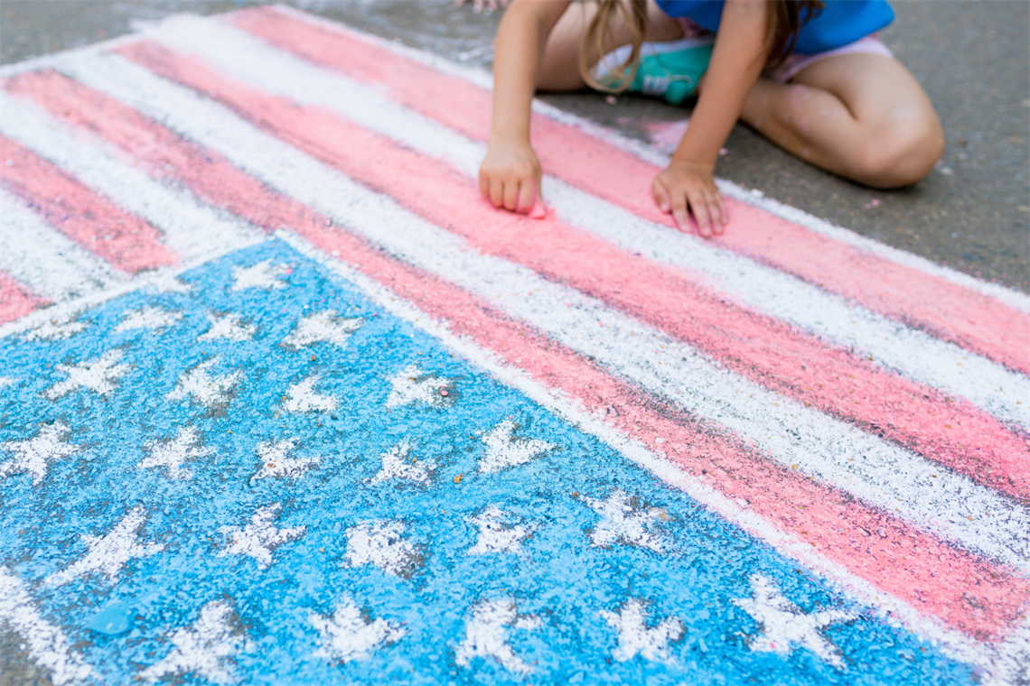 Child drawing an American flag using chalk on sidewalk