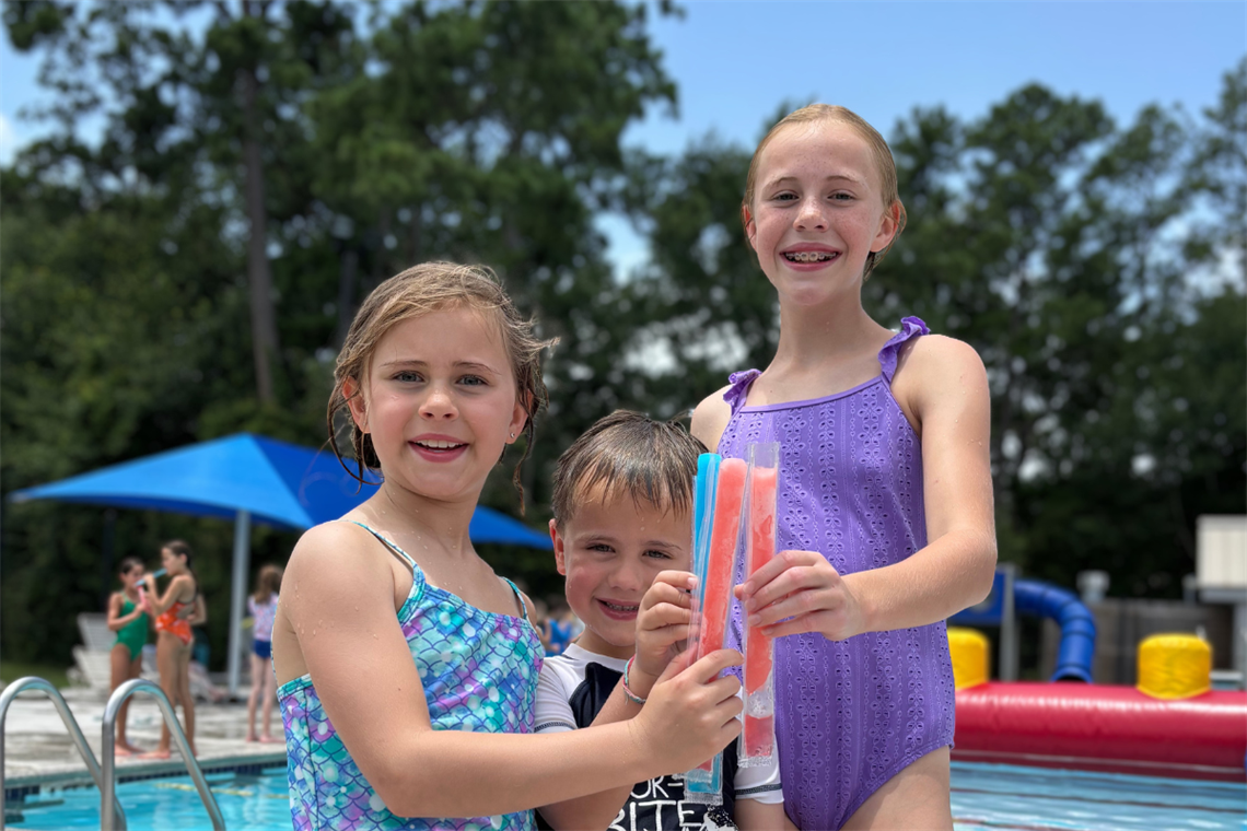 Three children smiling holding a popsicle at a pool